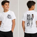 Бяла детска тениска CR7 с малък футболен принт отпред и ефектна графика RONALDO 07 на гърба.